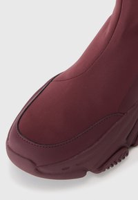Baskets montantes bordeaux avec une finition lisse et mate, dotées de coutures noires contrastantes et d'une semelle épaisse texturée pour l'adhérence.