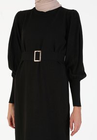 Abito nero con maniche lunghe a sbuffo e vita aderente. Presenta una cintura in tessuto con fibbia metallica rettangolare. Realizzato in materiale morbido.