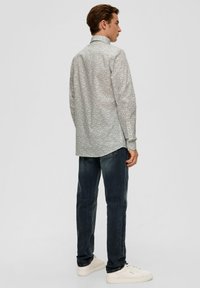 Helle Langarmbluse mit kleinen dunklen Druckmustern, mit Knopfleiste am Kragen und an den Manschetten. Kombiniert mit dunklen Jeans und weißen Sneakers.