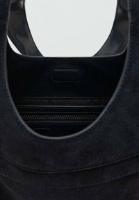 Czarna torba typu tote zamszowa z gładkim skórzanym wnętrzem, wyposażona w kieszeń na suwak oraz owalne wycięcia na rączki, ułatwiające przenoszenie.