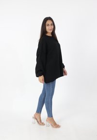 Maglione nero oversize con scollatura rotonda e spalle scese, abbinato a jeans skinny azzurri chiari e sandali con tacco a blocco trasparente.