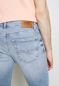 Hellblaue Jeans aus Denim mit taillierter Passform, ausgestattet mit Gesäßtaschen und einem braunen Leder-Label, auf dem "TOMMY JEANS" steht.