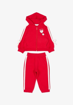 Giacca rossa con cappuccio, strisce laterali bianche, toppe a forma di cuore e pantaloni rossi coordinati con strisce bianche. Progettato per bambini.