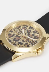 Montre dorée avec un cadran à imprimé léopard, ornée d'accents scintillants, de aiguilles blanches et d'un bracelet en silicone noir élégant.