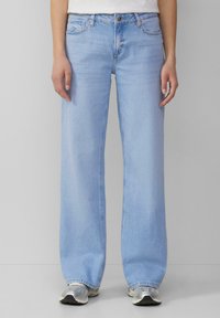 Šviesiai mėlyni plačiakojai džinsai su klasikinėmis penkiomis kišenėmis, turintys sagčių užtraukimą ir subtilų blukimą visame paviršiuje.