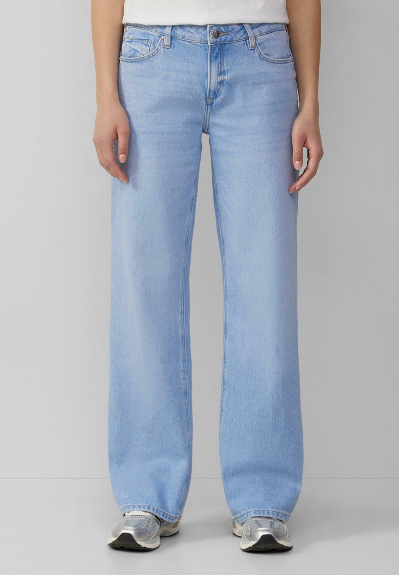 Šviesiai mėlyni plačiakojai džinsai su klasikinėmis penkiomis kišenėmis, turintys sagčių užtraukimą ir subtilų blukimą visame paviršiuje.