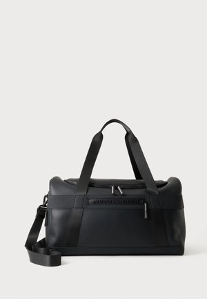 Musta Armani Exchange -laukku, jossa on kaksi kantokahvaa, irrotettava olkahihna ja etupuolella logo sileällä materiaalilla yksiväristä taustaa vasten.