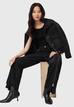 Zwarte denimjack met gouden hardware, zwarte tanktop en hoge zwarte jeans. Zwarte enkellaarsjes met een puntige neus maken de outfit compleet.