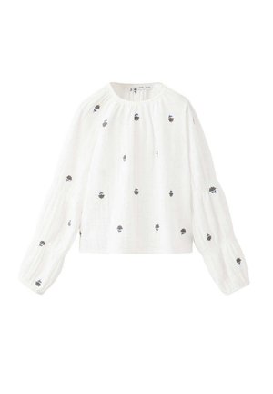Blouse blanche à manches longues avec manches larges et petites broderies florales noires et bleues éparses.