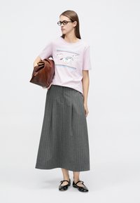 Ανοιχτό ροζ μπλουζάκι με γραφικό άλογο και μπλε ρίγες, συνδυασμένο με μακριά γκρι πλισέ φούστα. Καφέ τσάντα και μαύρα φλατ παπούτσια ολοκληρώνουν το σύνολο.