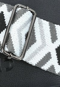 Schwarzes strukturiertes Material mit einem grau-weißen Zickzackmuster-Riemen, ausgestattet mit einer silbernen Metallbeschläge zur Befestigung.