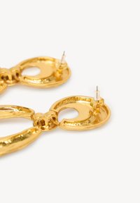 Gouden metalen oorbellen met een glanzende afwerking, voorzien van in elkaar verknopte ronde en langwerpige vormen, bevestigd met transparante stud-ankers.