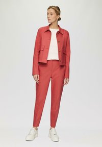 Veste rouge courte avec deux poches avant et des boutons, associée à un pantalon ajusté assorti et des baskets blanches à plateforme. Haut en tricot blanc en dessous.