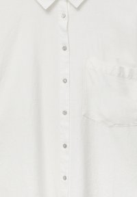 Chemise en lin blanc vue de face avec six boutons visibles et une poche poitrine unique sur le côté droit.