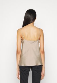 Top de seda beige con tirantes finos ajustables, forma fluida y textura suave, combinado con pantalones negros. Vista trasera mostrada.