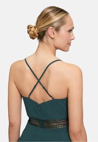 Robe turquoise avec un design de bretelles croisées dans le dos. Dotée d'une taille à motif en dentelle et d'une fermeture éclair dans le dos. Texture de tissu lisse.
