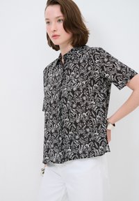 Camicia a maniche corte in tessuto nero con motivo floreale bianco, con chiusura a bottoni e vestibilità rilassata.