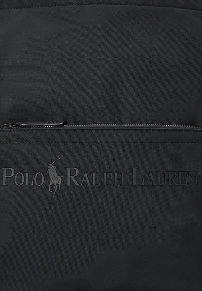 Must tekstureeritud kangas koos Polo Ralph Laureni logoga ja hobuse polo mängija embleemiga, mis on reljeefne horisontaalse tõmbluku kohal.