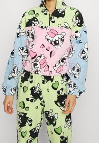 Fleece-Loungewear-Set mit einem Halbzip-Oberteil in pink, grün und blau mit Farbblöcken sowie gemusterten Hosen mit Cartoon-Charakteren und Herzen.
