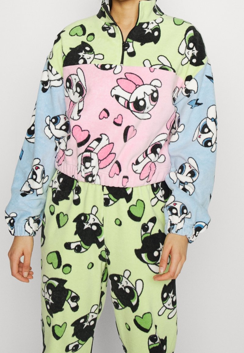 Fleece-Loungewear-Set mit einem Halbzip-Oberteil in pink, grün und blau mit Farbblöcken sowie gemusterten Hosen mit Cartoon-Charakteren und Herzen.