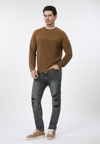 Sweat-shirt marron en maille avec motif texturé et col blanc, associé à un jean noir usé et des baskets marron clair avec semelles blanches.