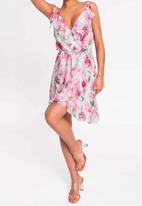 Květinové šaty na zavazování z lehké látky s růžovými a zelenými vzory. Mají volánkové ramínka a asymetrický lem. V kombinaci s průhlednými podpatky.