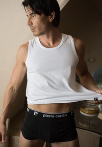 Débardeur en coton blanc et boxer noir avec un logo Pierre Cardin. Le débardeur présente un ajustement serré, mettant en valeur les bras et le torse musclés.