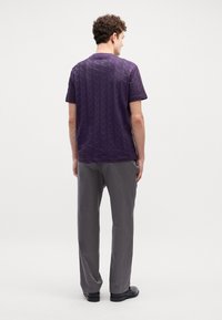 Camicia corta viola con un motivo geometrico testurizzato, abbinata a pantaloni grigi. L'outfit ha una vestibilità comoda ed è adatto per un look informale.