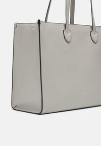 Sac tote en cuir gris avec une texture lisse, bord noir et double poignées. Présente une marque discrète en bas. Forme rectangulaire.