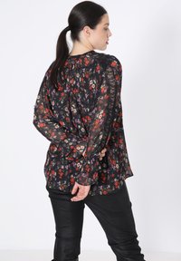 Black floral blouse with long, sheer sleeves, featuring red, purple, and yellow patterns. Textured fabric with a loose fit, back pleating detail.
