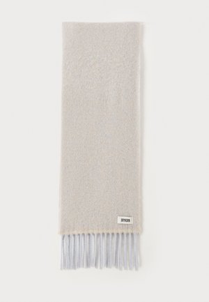 Écharpe gris clair en laine douce avec une texture lisse. Présente des franges dans une teinte légèrement plus claire. Étiquette logo dans le coin inférieur.