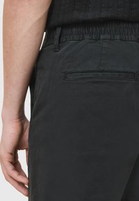 Pantaloni neri con vita elasticizzata, tasche laterali e tasca sul retro a filetto, con una finitura liscia, opaca e una texture sottile.