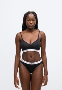 Černá braletka a set tanga s tenkými ramínky a elastickým páskem s logem "TOMMY HILFIGER" v kontrastních bílých a červených barvách.