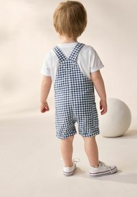 Blå och vit rutiga overaller med justerbara hängslen, ihop med en vit t-shirt och vita sneakers, med en rund vit boll i närheten.