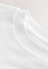 Gros plan d'un t-shirt blanc uni à col rond montrant la texture du tissu et les coutures du col.