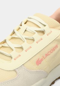 Yellow mesh sneaker with cream accents, round laces, and pink logo. Textured surface and smooth suede panel detailing on the sides.