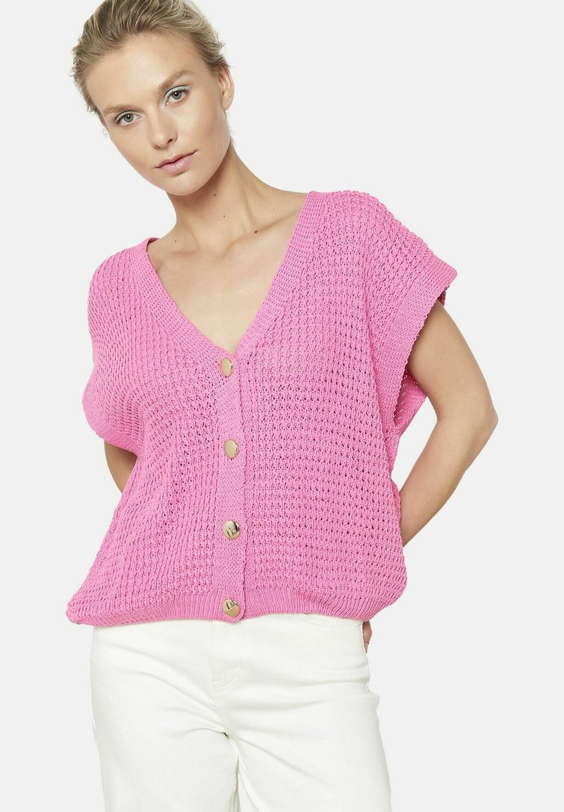 Rozā adīta džemperis ar V-veida kakla izgriezumu, īsām piedurknēm un divām zelta pogām priekšpusē. Brīvi teksturēts audums, relaksēta piegriezte.