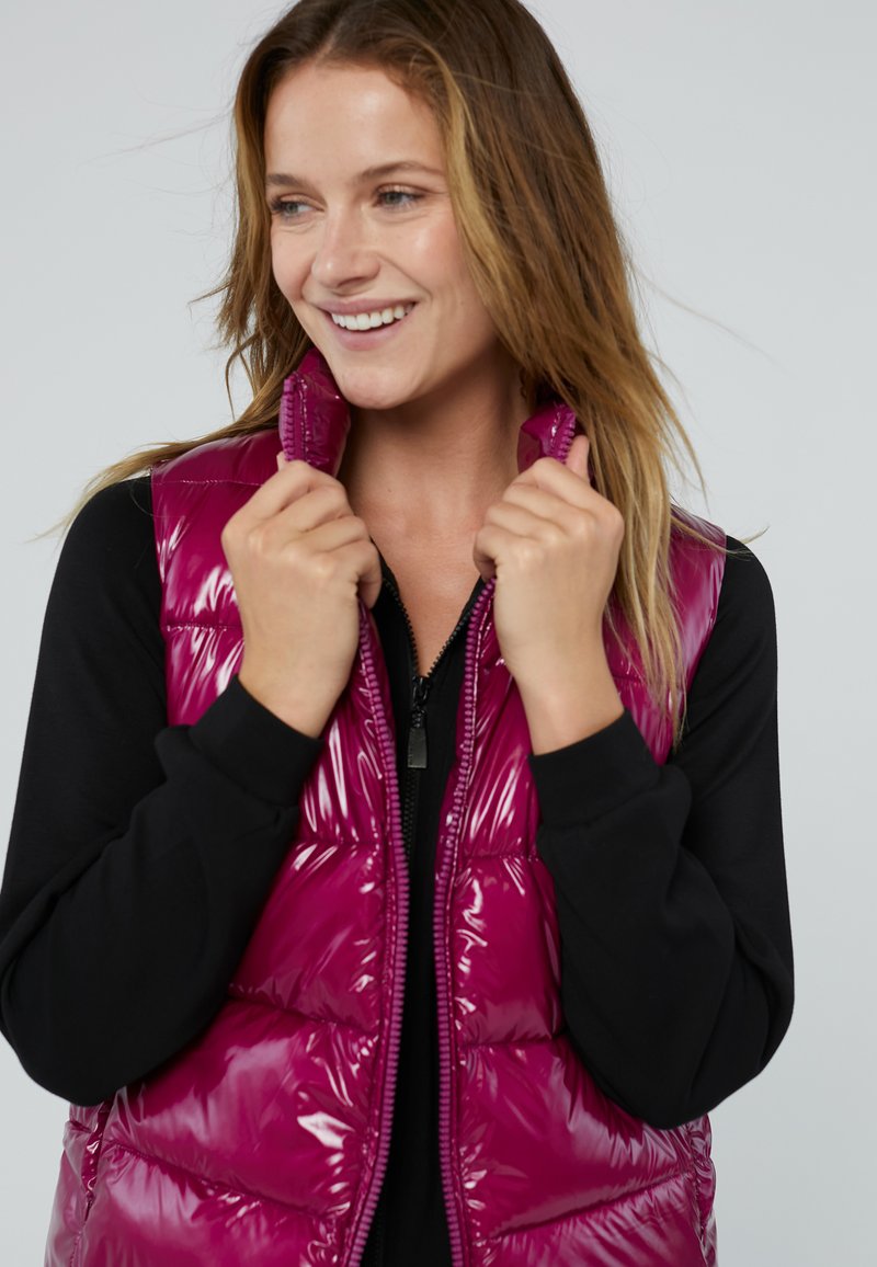 Glanzende fuchsia puffer vest met ritssluiting en hoge kraag, met gestikte horizontale panelen. Gemaakt over een zwart langemouwtop.