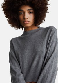 Szary sweter dzianinowy z prążkowanym, okrągłym dekoltem, opuszczanymi ramionami i luźnym krojem. Miękka tekstura, długie rękawy i krótka długość.