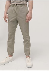 Ljust grå joggers med elastisk midja, dragsnöre och uppvikta anklar. Bärs med vita sneakers, slät textur.