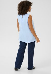 Haut sans manches bleu clair avec un détail à découpe en forme de clé au dos, associé à un jean droit bleu foncé et des chaussures plates noires.