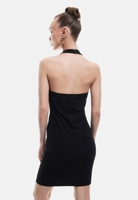 Musta halterneck-mekko, tiukka muotoilu, polven pituinen. Sileä rakenne, minimaalinen yksityiskohtaus, takaosassa napitus.