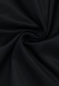 Tessuto nero con una superficie liscia e leggermente texture, attorcigliato a spirale, che mostra un colore scuro uniforme e una leggera lucentezza.