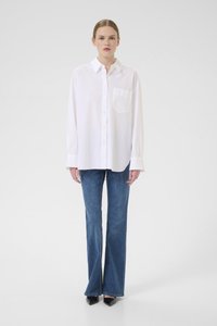 White button-up shirt with long sleeves, single chest pocket. Paired with flared blue denim jeans. Model wears black pointed-toe heels.
