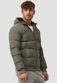 Olijfgroene pufferjack met een bruine fleece- gevoerde capuchon, rits aan de voorkant en zijzakken. Getextureerde stof met ribbels aan de manchetten en zoom.