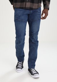 Denimjeans i mörkblått med rak passform, med subtila sömdetaljer och tre framfickor. Matchas med svartvita sneakers.
