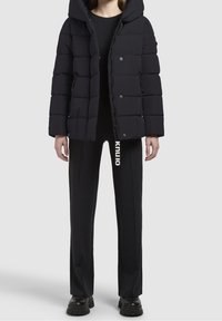 Musta toppatakki, jossa on huppu, tikattu malli ja nepparikiinnitys. Yhdistetty mustiin housuihin, joissa on pystysuora valkoinen logo.