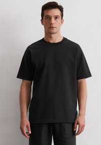 Zwarte katoenen t-shirt met korte mouwen, ronde hals, relaxte pasvorm, voorzien van een zijlabelaccent. Gladde textuur en minimalistisch ontwerp.