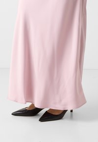 Tessuto di un vestito fluido di un rosa chiaro, con una superficie liscia, abbinato a scarpe con punta nera e tacco leggero, dotate di lati aperti.