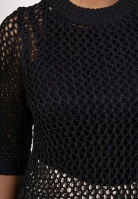 Haut en tricot noir avec un design en maille, manches courtes, col côtelé et une couche de base unie. La texture est ouverte et respirante.